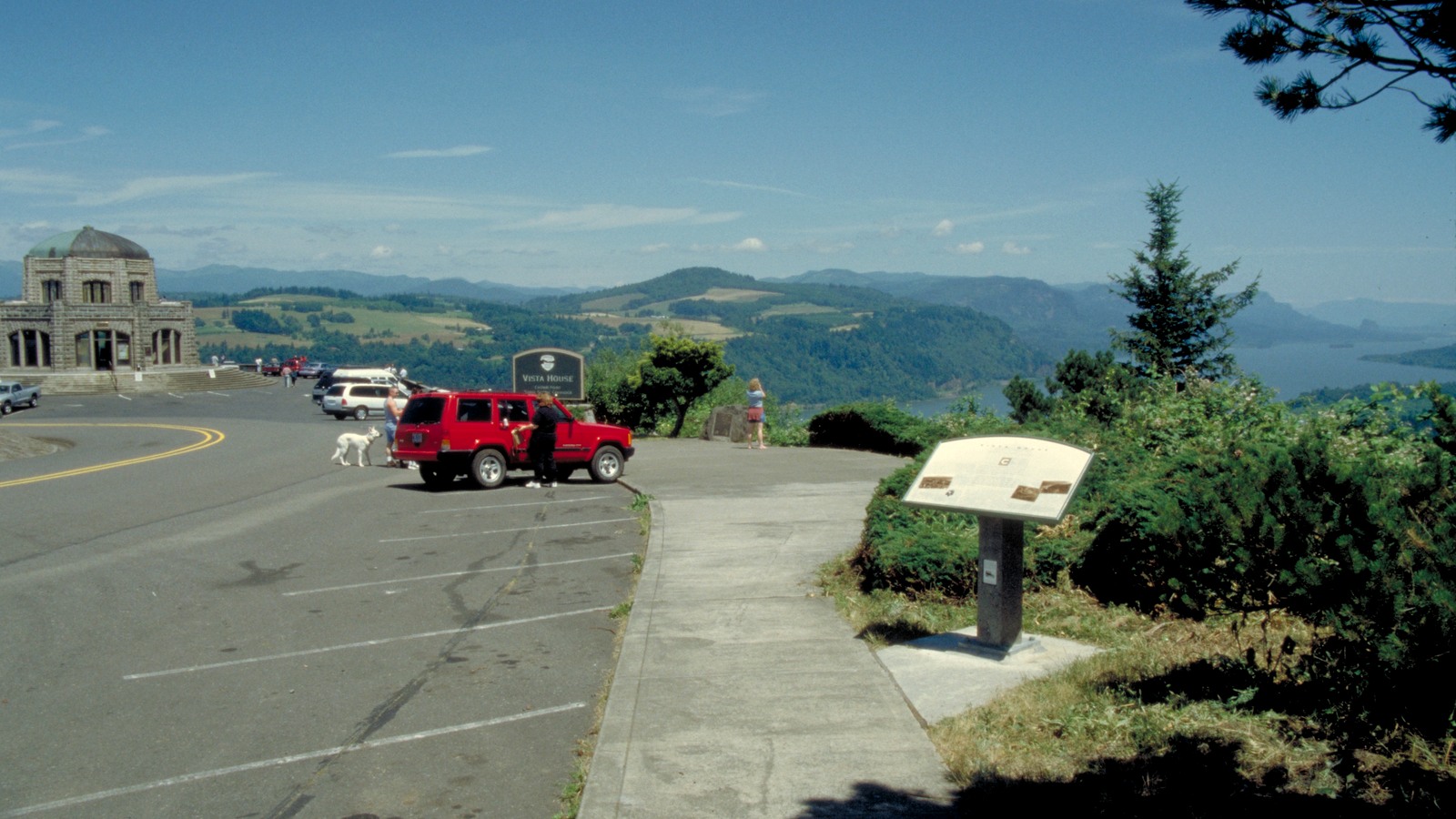 Cars parked beside Vista House at Crown Point, with the Columbia River Gorge visible in the distance.